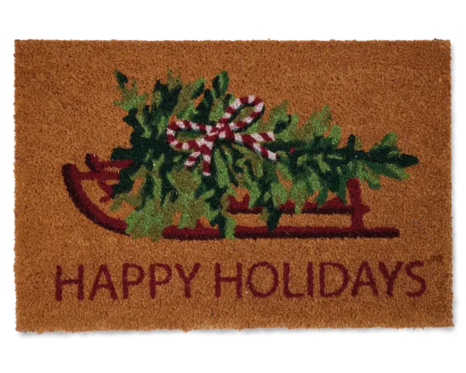 Rektangulært dørmåtte af kokosfiber med et festligt motiv af en rød slæde, der bærer grønne julegrene bundet med en rød- og hvidstribet sløjfe. Nederst står teksten 'HAPPY HOLIDAYS' med store røde bogstaver. Måtten har en naturlig brun baggrund og en tekstureret overflade, der hjælper med at fjerne snavs fra sko.