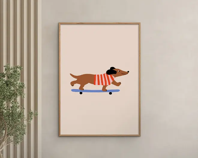 Minimalistisk illustration af en brun gravhund iført en rød- og hvidstribet sweater og sort beret, der kører på et blåt skateboard. Baggrunden er ensfarvet lysebeige, og kunstværket er indrammet i en enkel træramme.