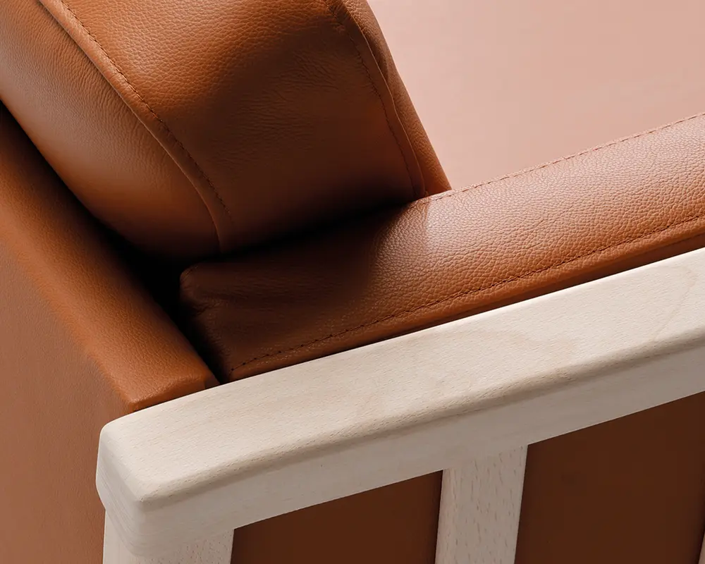 Nærbillede af et møbel med en glat, lysebrun læderhynde med synlige syninger, placeret på en lys træramme. Læderet ser blødt og let tekstureret ud, mens træet har et naturligt, ubehandlet udseende med rene linjer og afrundede kanter.