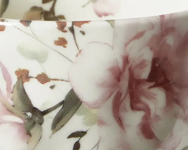 Nærbillede af en keramisk overflade med et fint blomsterdesign. Mønsteret viser store, bløde lyserøde og bordeaux blomster med grønne blade og brune stilke på en hvid baggrund. Blomsterne er detaljeret med bløde nuancer, hvilket giver et akvarel-lignende udtryk, og det samlede look er elegant og raffineret.