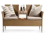 To-personers bænk lavet af flettet rattan med indbygget centertable. Bænken har to tykke, lyse sædehynder og to store pyntepuder med grå og hvide striber. Centertablet har en flad overflade med drikkevarer og snacks samt en åben hylde nedenunder, hvor der ligger en bog. Benene er slanke og har metalforstærkede fødder for ekstra stabilitet.