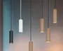 Et sæt af seks cylinderformede pendellamper med et moderne, minimalistisk design. Lamperne har en lodret rillet overflade og fås i tre forskellige finish: mat sort, mat hvid og børstet guld. Hver lampe hænger i en tynd ledning, hvor ledningens farve matcher lampen. Lamperne er ophængt i forskellige højder, hvilket skaber et visuelt dynamisk udtryk. Den åbne bund giver et fokuseret, nedadrettet lys.