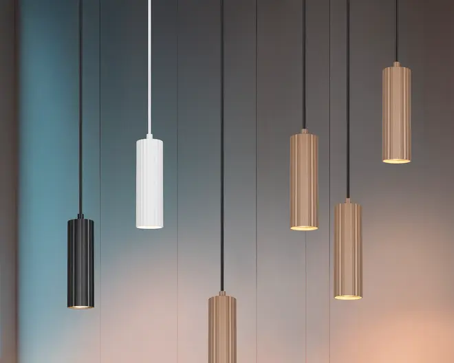 Et sæt af seks cylinderformede pendellamper med et moderne, minimalistisk design. Lamperne har en lodret rillet overflade og fås i tre forskellige finish: mat sort, mat hvid og børstet guld. Hver lampe hænger i en tynd ledning, hvor ledningens farve matcher lampen. Lamperne er ophængt i forskellige højder, hvilket skaber et visuelt dynamisk udtryk. Den åbne bund giver et fokuseret, nedadrettet lys.