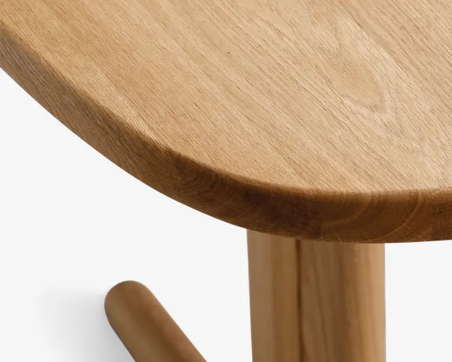 Nærbillede af en glat, afrundet trækant med naturlig finish. Træets årer er synlige, og håndværket fremhæver en sømløs, poleret overflade. Benet og støttearmen er også lavet af matchende træ, hvilket giver et ensartet og solidt udtryk.