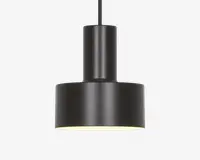 En moderne pendellampe med en mat sort, cylindrisk krop og en bred, flad bundskærm. Designet er minimalistisk med rene linjer og en glat overflade. Lampens inderside er hvid, hvilket hjælper med at reflektere lyset nedad for fokuseret belysning. Lampen hænger fra en lige sort ledning eller stang.