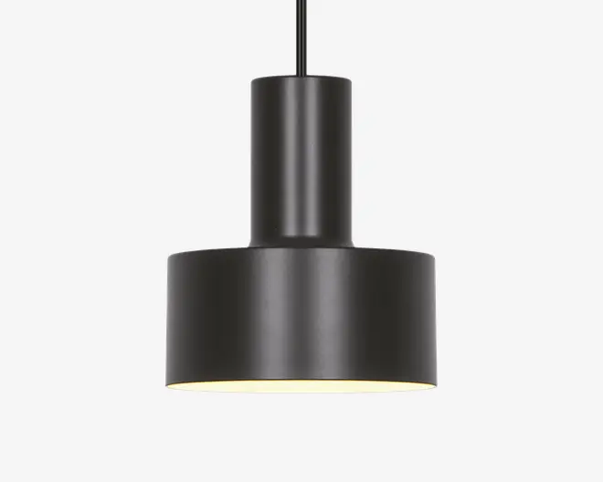 En moderne pendellampe med en mat sort, cylindrisk krop og en bred, flad bundskærm. Designet er minimalistisk med rene linjer og en glat overflade. Lampens inderside er hvid, hvilket hjælper med at reflektere lyset nedad for fokuseret belysning. Lampen hænger fra en lige sort ledning eller stang.