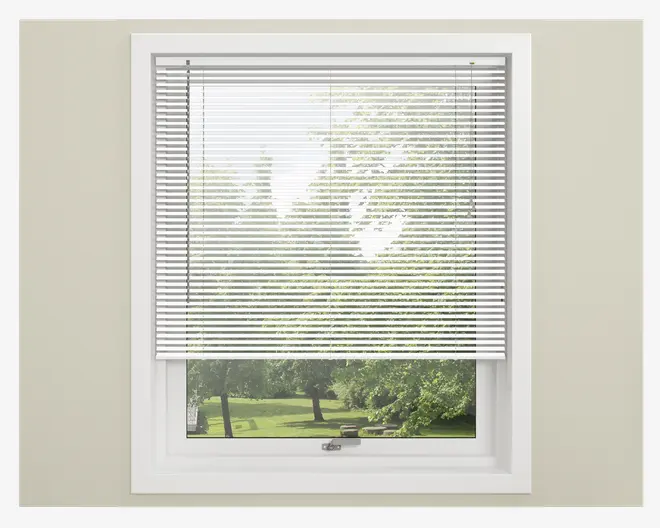 Hvide vandrette lamelgardiner, der er delvist trukket ned foran et vindue og lader filtreret lys komme ind. Gardinet har jævnt fordelte, tynde lameller og er monteret inden for en hvid vinduesramme. Betjeningssnore ses på begge sider til justering af gardinets højde og vinkel.