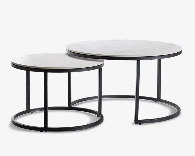 Sæt med to runde indskudsborde med hvide bordplader i marmorlook og slanke sorte metalstel. Det største bord er lidt højere og bredere, så det mindre bord kan skubbes delvist ind under for pladsbesparende opbevaring. Begge borde har et minimalistisk, moderne design med åbne, cirkulære baser, der giver et let og luftigt udtryk.