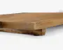 Nærbillede af en træoverflade med naturlig finish, der viser træets tykkelse og årer. Kanten er let skrå, og der er en forhøjet støtte underneden, hvilket indikerer en solid konstruktion. Træet har en varm, lysebrun farve med synlig struktur og diskrete farvevariationer.