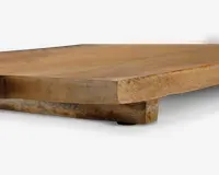 Nærbillede af en træoverflade med naturlig finish, der viser træets tykkelse og årer. Kanten er let skrå, og der er en forhøjet støtte underneden, hvilket indikerer en solid konstruktion. Træet har en varm, lysebrun farve med synlig struktur og diskrete farvevariationer.