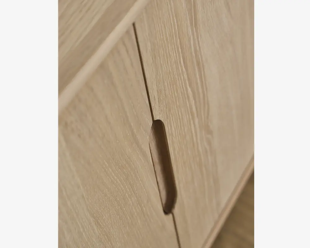 Nærbillede af en skabslåge lavet af lyst træ med naturligt åremønster. Lågen har et lodret, indfældet greb, der er udskåret direkte i træet for et minimalistisk og moderne udtryk. Kanterne er glatte, og overfladen fremstår mat.