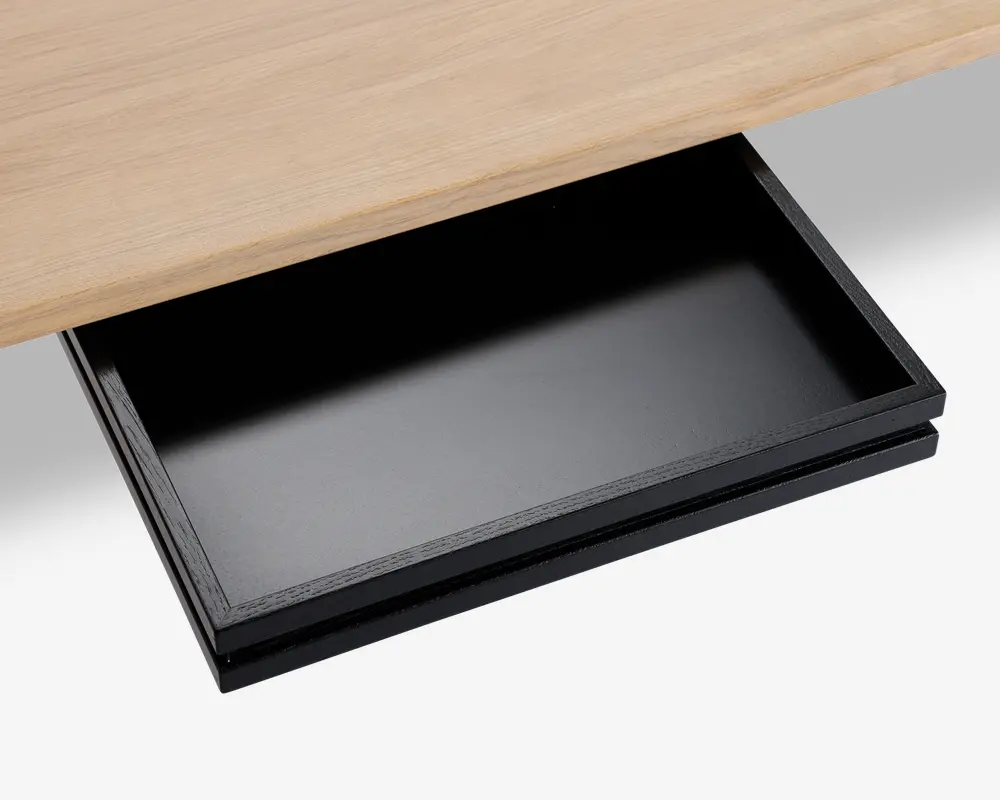 Et nærbillede af en elegant, sort underskuffe monteret under en bordplade i lyst træ. Skuffen er rektangulær, har en glat, mat overflade og er vist helt udtrukket, hvilket giver god opbevaringsplads til små kontorartikler eller personlige ejendele. Designet er minimalistisk og moderne og passer diskret sammen med bordet.