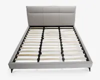 Moderne sengegavl med lysegråt polstret hovedgærde, der har tre store rektangulære paneler. Rammen har en lav profil med matchende gråt stof på siderne og fodenden. Bunden består af jævnt fordelte lameller i træ, som understøttes af en sort metalstruktur, hvilket gør det muligt at bruge sengen uden boxmadras. Sengen står på korte, skrå sorte ben.