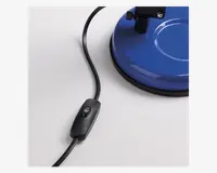 Nærbillede af en sort ledningsafbryder monteret på en strømkabel, placeret ved siden af en rund blå base med sort kant. Afbryderen har en enkel tænd/sluk-knap, og basen har en glat, blank overflade med en cirkulær fordybning.