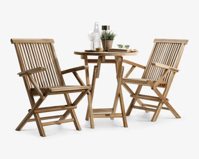Sættet består af to træstole og et rundt træbord, alle med en naturlig finish. Stolene har lamel-ryg og -sæde, armlæn og kan foldes sammen for nem opbevaring. Bordet har et robust krydsben og en lav hylde for ekstra stabilitet. På bordet står dekorative genstande, herunder en glasflaske, en lille potteplante, et stearinlys og et par solbriller, hvilket antyder en afslappet udendørs stemning.