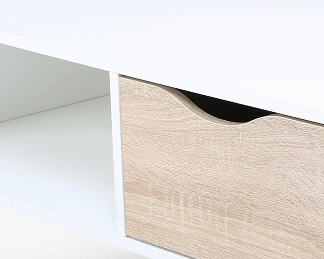 Nærbillede af et møbel med hvid ramme, åben hylde til venstre og en skuffe med lyst trælook til højre. Skuffen har et buet udskåret greb øverst for nem åbning. Designet er moderne og minimalistisk.