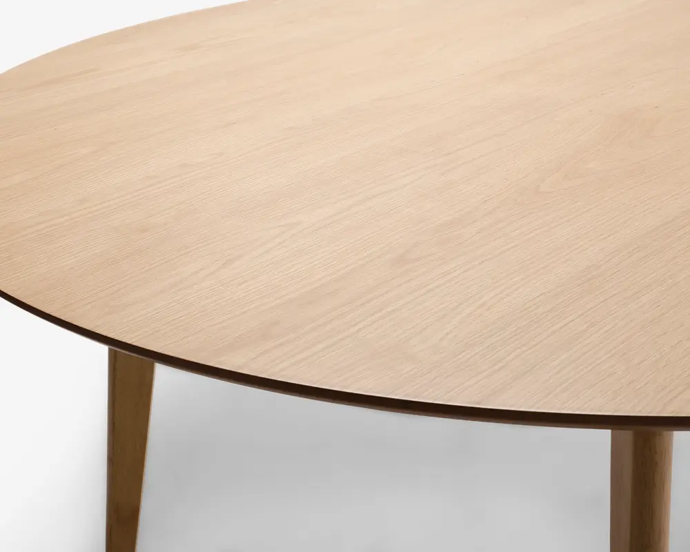 Rund bordplade med en lys, naturlig træfinish og synlig træstruktur, understøttet af slanke, koniske træben. Bordpladens kant er tynd og let affaset, hvilket giver et moderne og minimalistisk udtryk.