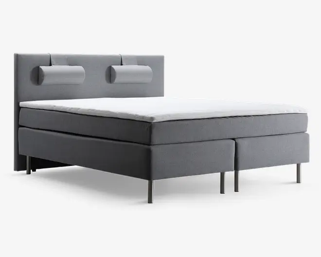 Moderne seng med lysegråt polstret stel og hovedgærde. Hovedgærdet har to vandrette, cylindriske pøllepuder fastgjort. Sengen har et firkantet, minimalistisk design med rene linjer og står på seks slanke, metalben. Madrassen er tyk og blød og har en hvid topmadras for ekstra komfort.