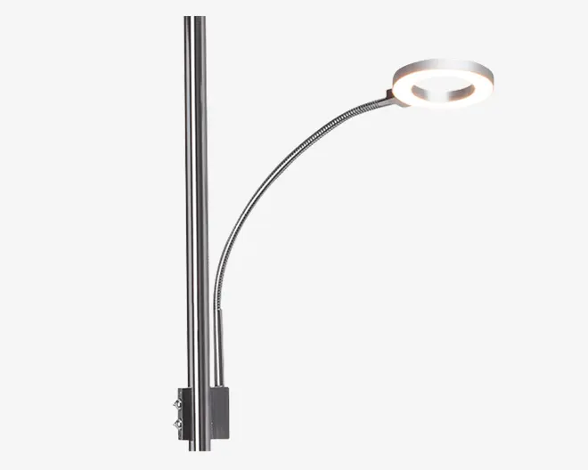 En moderne, metallisk lampe med en slank, lodret monteringsstang og en fleksibel, buet svanehalsarm. Lampens hoved er cirkulært med et åbent center og udsender lys i en ringform. Overfladen er blank krom, hvilket giver et stilrent og moderne udtryk.