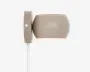 En moderne vægmonteret lampe med en glat, mat taupe-farvet overflade. Lampen har en ovalt formet skærm, der leder lyset nedad, samt en rektangulær vægplade med en synlig skrue til montering. En hvid ledning går ud fra bunden af vægpladen. Designet er minimalistisk og moderne, velegnet til forskellige indretninger.