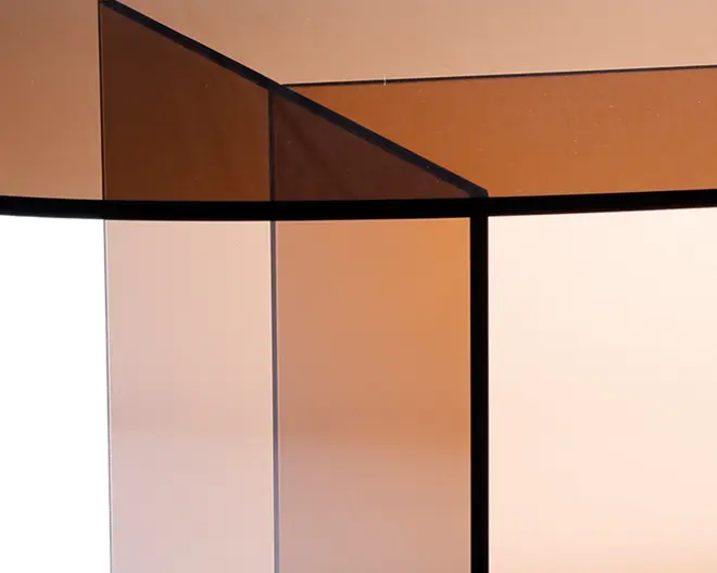 Nærbillede af en geometrisk struktur lavet af tonede glasplader med sorte metalrammer. Glasset har en gradienteffekt, der går fra mørkere ravfarvet øverst til en lysere nuance nederst. De rene linjer og skarpe vinkler giver et moderne, minimalistisk udtryk.