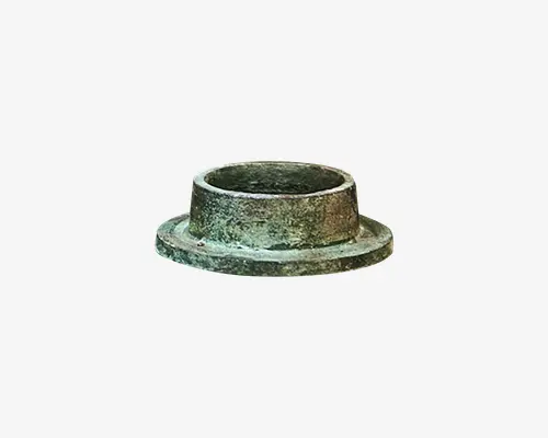 En cylindrisk metalbøsning med en bred, flad flange i bunden. Overfladen har en ru, tekstureret finish med et grønligt skær, hvilket tyder på, at den kan være lavet af bronze eller en lignende legering. Det indvendige hul er glat og rundt, egnet til montering omkring en aksel eller stang.