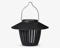 Sort lanterne-lignende enhed med bred, skrånende top og lodrette lameller, der udgør kroppen. Den har et buet metalhåndtag til ophængning og en mat overflade. Designet giver luftgennemstrømning gennem lamellerne, og toppen beskytter ovenfra.