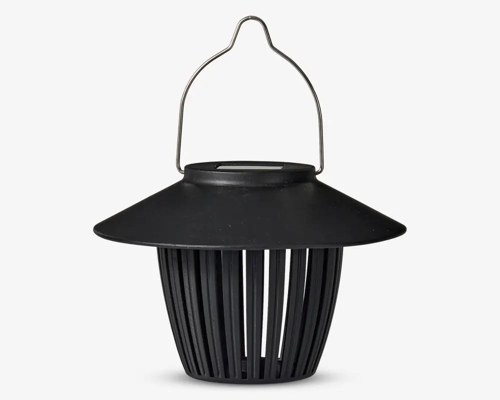 Sort lanterne-lignende enhed med bred, skrånende top og lodrette lameller, der udgør kroppen. Den har et buet metalhåndtag til ophængning og en mat overflade. Designet giver luftgennemstrømning gennem lamellerne, og toppen beskytter ovenfra.