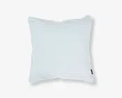 Firkantet pude med et diskret, fint lyseblåt og hvidt nålestribet mønster. Stoffet ser blødt og glat ud, og puden har et let overfyldt, fyldigt udseende. Der er et lille sort stofmærke på den ene kant, sandsynligvis med mærkets navn. Kanterne er pænt afsluttede med en let piping-detalje.