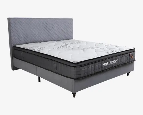Moderne seng med høj, quiltet grå sengegavl og en tyk madras med hvid top og diskrete bølgemønstre. Madrassen har sort sidepanel med gitterstruktur og mærket 'SWEETNIGHT' broderet på siden. Sengebunden er polstret med gråt stof og står på metalben.