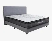 Moderne seng med høj, quiltet grå sengegavl og en tyk madras med hvid top og diskrete bølgemønstre. Madrassen har sort sidepanel med gitterstruktur og mærket 'SWEETNIGHT' broderet på siden. Sengebunden er polstret med gråt stof og står på metalben.