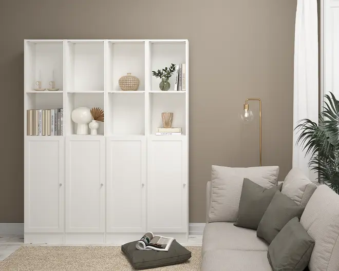 Høj, hvid reolenhed med fire sektioner, hver med to åbne hylder øverst og et lukket skab med låge nederst. De åbne hylder viser dekorative genstande som bøger, vaser, en lille plante og moderne skulpturer. Enheden har et rent, minimalistisk design med enkle runde greb på skabslågerne.