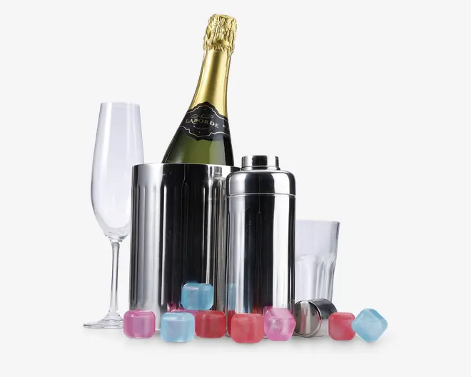 Billedet viser et sæt barudstyr, herunder en champagnekøler i rustfrit stål med en flaske champagne, en matchende cocktailshaker med låg, et klart champagneglas, et klart tumblerglas og flere genanvendelige isterninger i pink, blå og røde farver. Produkterne er arrangeret sammen og fremhæver det blanke metal og de farverige isterninger.