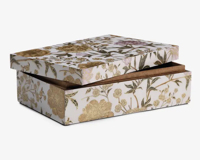 Rektangulær æske med aftageligt låg, dekoreret med et hvidt baggrund og detaljerede blomster-mønstre i guld og grønne nuancer. Æsken har en blank overflade, og blomsterdesignet dækker alle synlige flader, hvilket giver et elegant og dekorativt udtryk. Indersiden ser ud til at være foret med et brunt materiale.