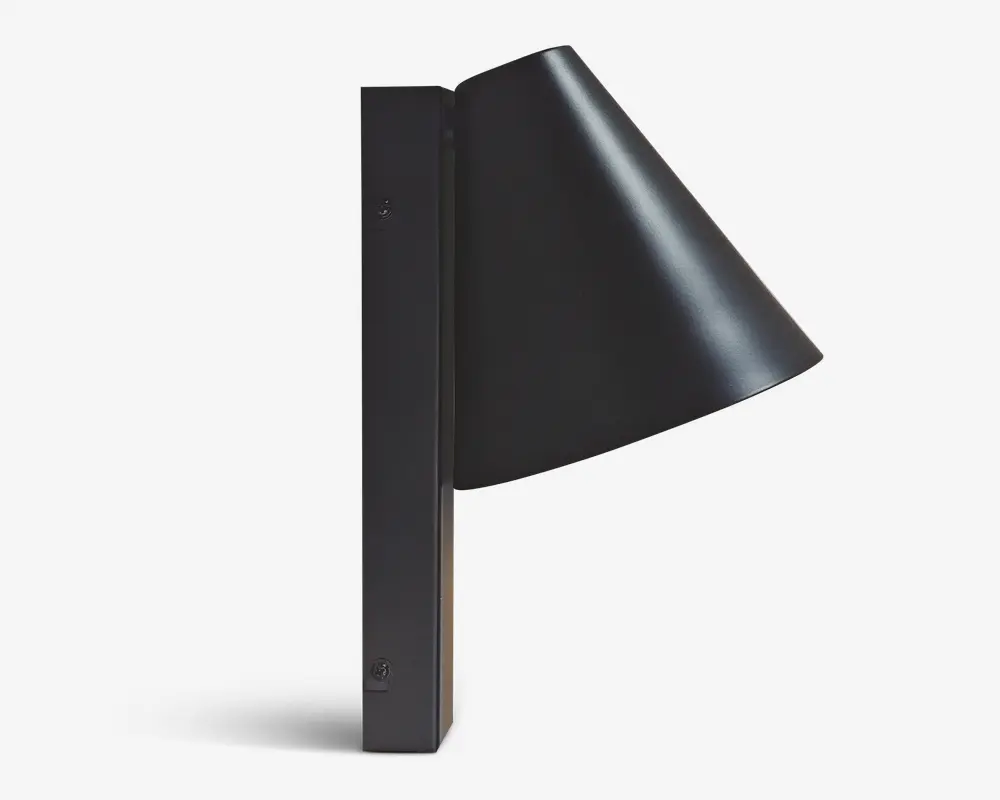 En moderne vægmonteret lampe med mat sort finish. Lampen har en konisk skærm, der leder lyset nedad, og er fastgjort til en rektangulær, lodret base. Designet er minimalistisk og stilrent, velegnet til moderne indretning.