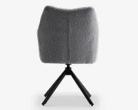 Billedet viser bagsiden af en stol med et buet, polstret ryglæn betrukket med et tekstureret gråt stof. Stolen har et moderne design med en central sort metalbase og fire skråtstillede ben, der giver stabilitet. Polstringen ser blød og fyldig ud, og der er en synlig syning, der løber lodret ned langs midten af ryglænet.