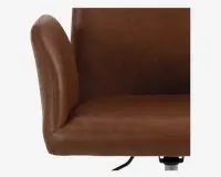 Nærbillede af en stol med glat brun kunstlæderpolstring, let buet ryglæn og tykt polstret sæde. Syningerne er synlige langs kanterne og giver et elegant udtryk. Stolen har et moderne design med afrundede former og en robust base, der delvist kan ses nederst.