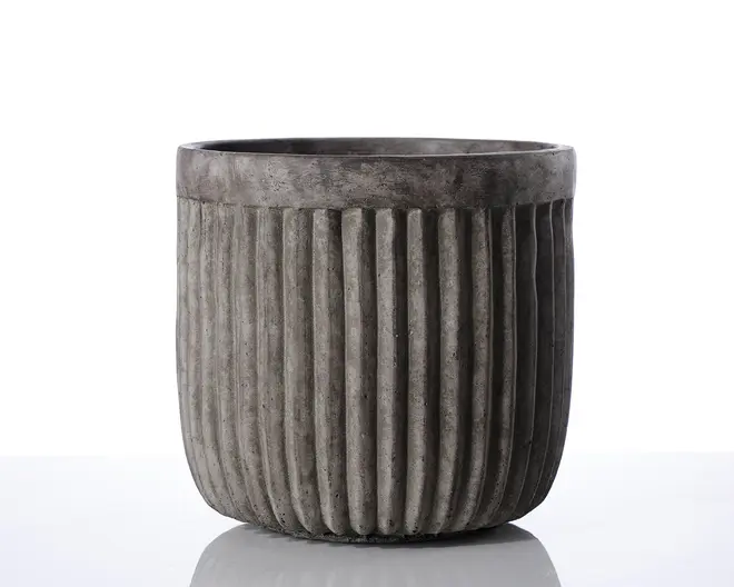 En cylindrisk beholder lavet af mørkegrå beton med mat overflade. Ydersiden har jævnt fordelte lodrette riller, der løber fra top til bund og giver en rillet tekstur. Kanten er glat og en smule tykkere end selve kroppen, og det samlede design er moderne og minimalistisk.