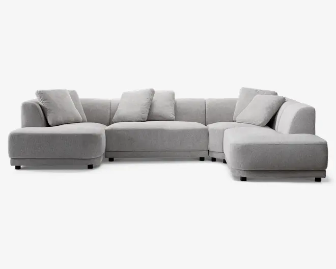 Stor, moderne hjørnesofa i lysegråt stof med lav profil og rene linjer. Sofaen har brede, dybe sæder og bløde ryghynder for ekstra komfort. Inkluderer fem matchende pyntepuder. Sofaen har en venstrevendt chaiselong og en højrevendt udvidet siddeplads, hvilket giver en L-formet opstilling.