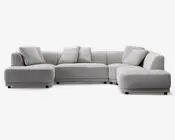 Stor, moderne hjørnesofa i lysegråt stof med lav profil og rene linjer. Sofaen har brede, dybe sæder og bløde ryghynder for ekstra komfort. Inkluderer fem matchende pyntepuder. Sofaen har en venstrevendt chaiselong og en højrevendt udvidet siddeplads, hvilket giver en L-formet opstilling.