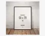 Rektangulær ramme med en tynd, sort kant, der passer til billeder i størrelsen 50 x 70 cm (B2). Rammen har et moderne, minimalistisk design og står op ad en hvid, let ru væg på et trægulv. Fronten er klar glas eller akryl, og rammen har en glat, mat overflade.
