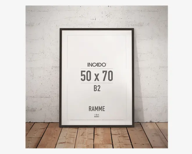Rektangulær ramme med en tynd, sort kant, der passer til billeder i størrelsen 50 x 70 cm (B2). Rammen har et moderne, minimalistisk design og står op ad en hvid, let ru væg på et trægulv. Fronten er klar glas eller akryl, og rammen har en glat, mat overflade.