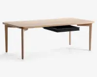 Rektangulært bord med lys træfinish, afrundede hjørner og koniske ben. Bordet har en diskret sort udtræksskuffe under bordpladen, som giver skjult opbevaringsplads og bevarer det minimalistiske og moderne design.