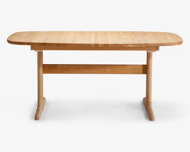 Rektangulært bord i lyst træ med afrundede hjørner og en glat bordplade, hvor træets årer er synlige. Bordet har to solide, buede ben, der er forbundet med en vandret støttebjælke for ekstra stabilitet. Designet er minimalistisk og moderne, velegnet til spise- eller arbejdsbrug.