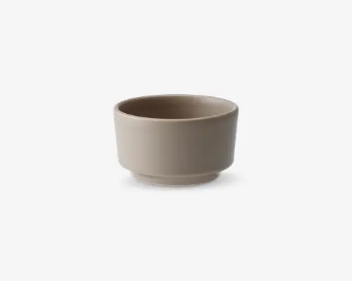 En lille, rund skål med en glat, mat overflade i en neutral beige farve. Skålen har lige sider og en let hævet bund, hvilket giver et moderne og minimalistisk udtryk. Kanten er let afrundet for et behageligt greb.