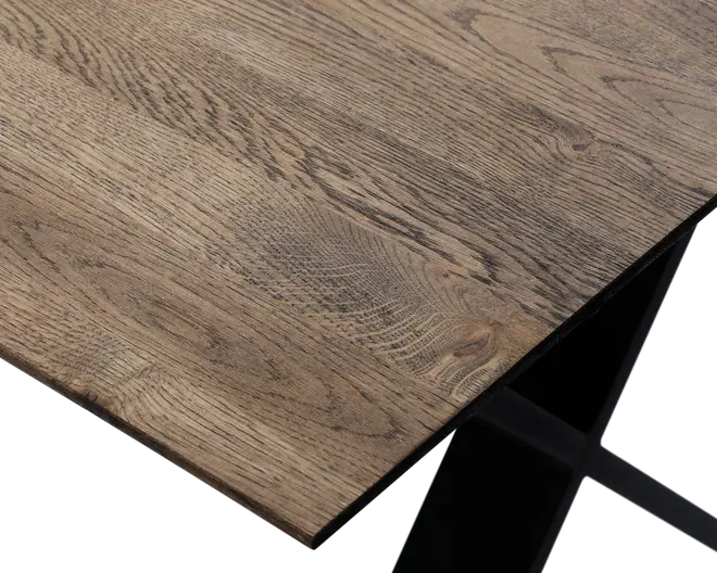 Nærbillede af en bordplade med naturlig træstruktur og let skrå kant. Overfladen viser forskellige træmønstre og knaster, hvilket giver et rustikt og autentisk udseende. Bordet understøttes af et solidt, sort metalben med et moderne, vinklet design.