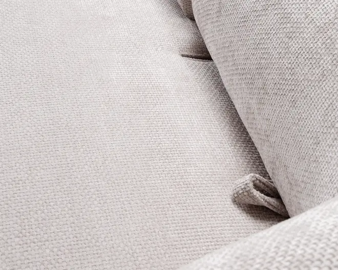 Nærbillede af et lysebeige stof med en tekstureret, vævet overflade. Materialet ser blødt og slidstærkt ud med synlige syninger og knapdetaljer, der bidrager til komfort og stil. Billedet viser også en matchende pude, hvilket indikerer et koordineret design og god støtte.