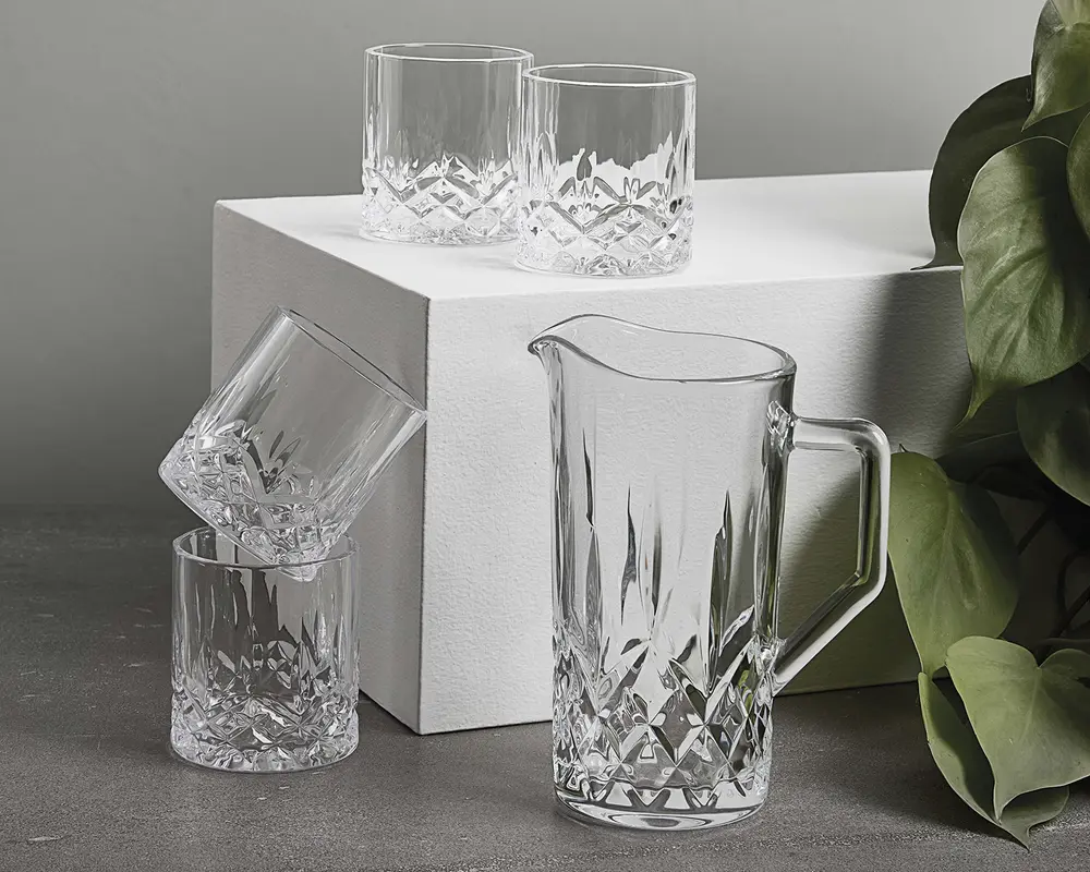 Sæt af klart glas, bestående af en kande og fire tumblere, alle med et facetslebet diamantmønster i bunden og lodrette snit opad. Kanden har et solidt håndtag og en hældetud for nem servering. Glassene er lave og brede, hvilket giver et behageligt greb. Glassættet har et klassisk og elegant udseende, velegnet til servering af drikkevarer ved både formelle og uformelle lejligheder.