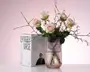 En klar, rillet glasvase med cylindrisk form, fyldt med vand og arrangeret med lyserøde roser og fint grønt løv. Vasens lodrette riller giver tekstur og elegance. Emballagen i baggrunden viser mærket 'Lyngby Vase' og angiver, at vasen er 20 cm høj. Udtrykket er moderne og minimalistisk, velegnet til nutidig boligindretning.