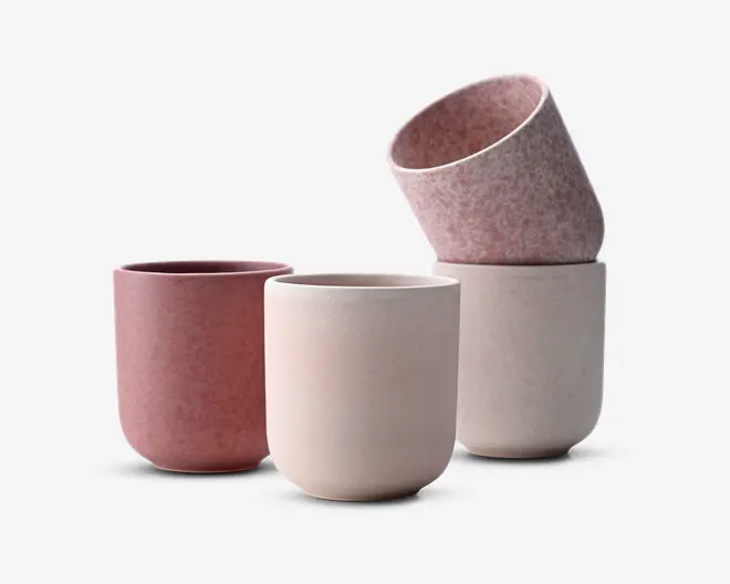 Sæt med fire cylindriske kopper med en glat, mat overflade. To kopper er i en afdæmpet rosa farve, og to er i en blød offwhite. Kopperne har et minimalistisk design uden hank eller dekorationer og let afrundede bunde. En rosa kop er stablet skråt oven på en offwhite kop, hvilket viser den indvendige tekstur.